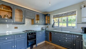 Una cocina con armarios grises, estufa a gas, horno empotrado y ventana con vistas al exterior.