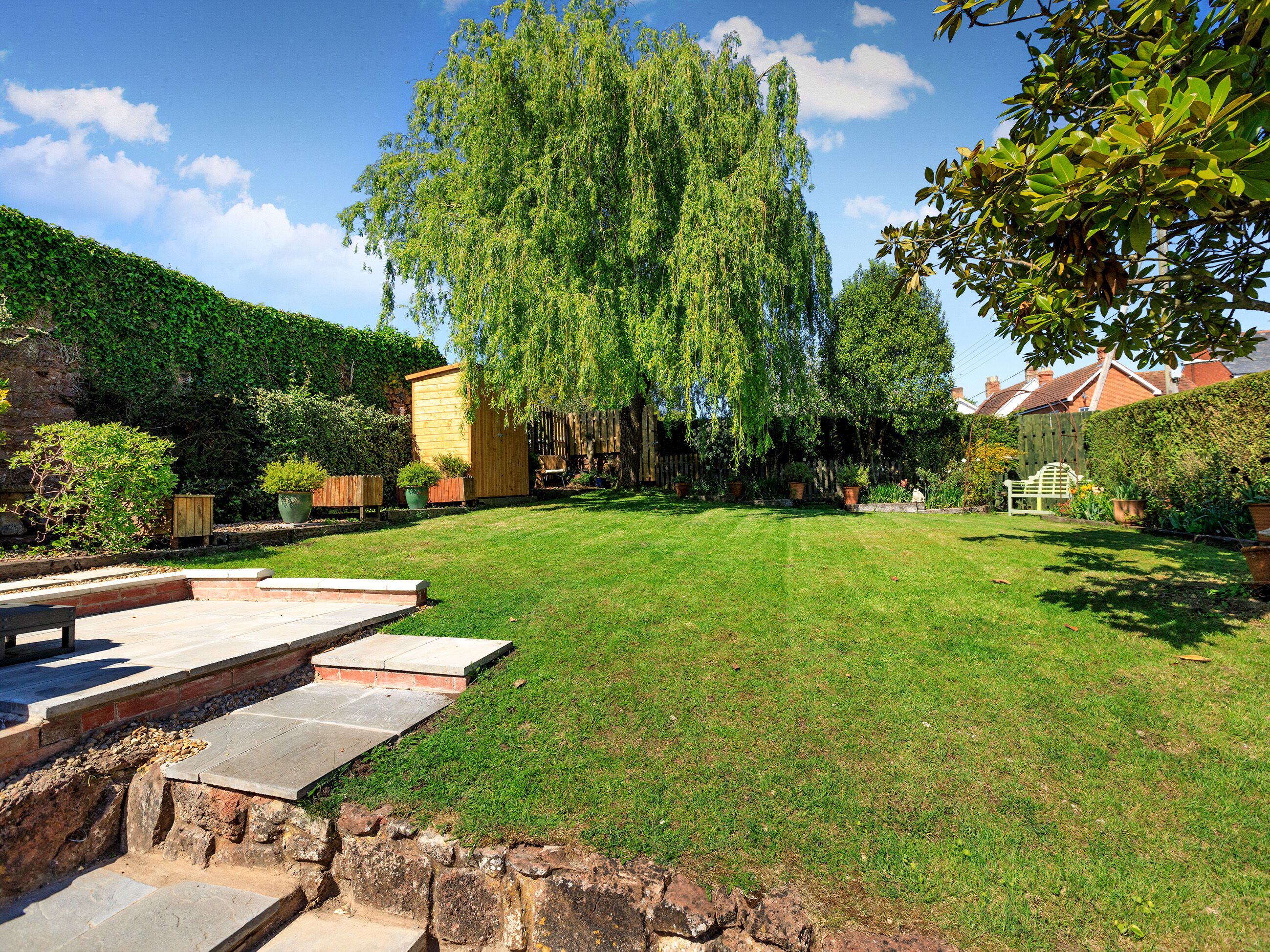 A well-maintained backyard with a wooden shed, a lawn, and a stone retaining wall.