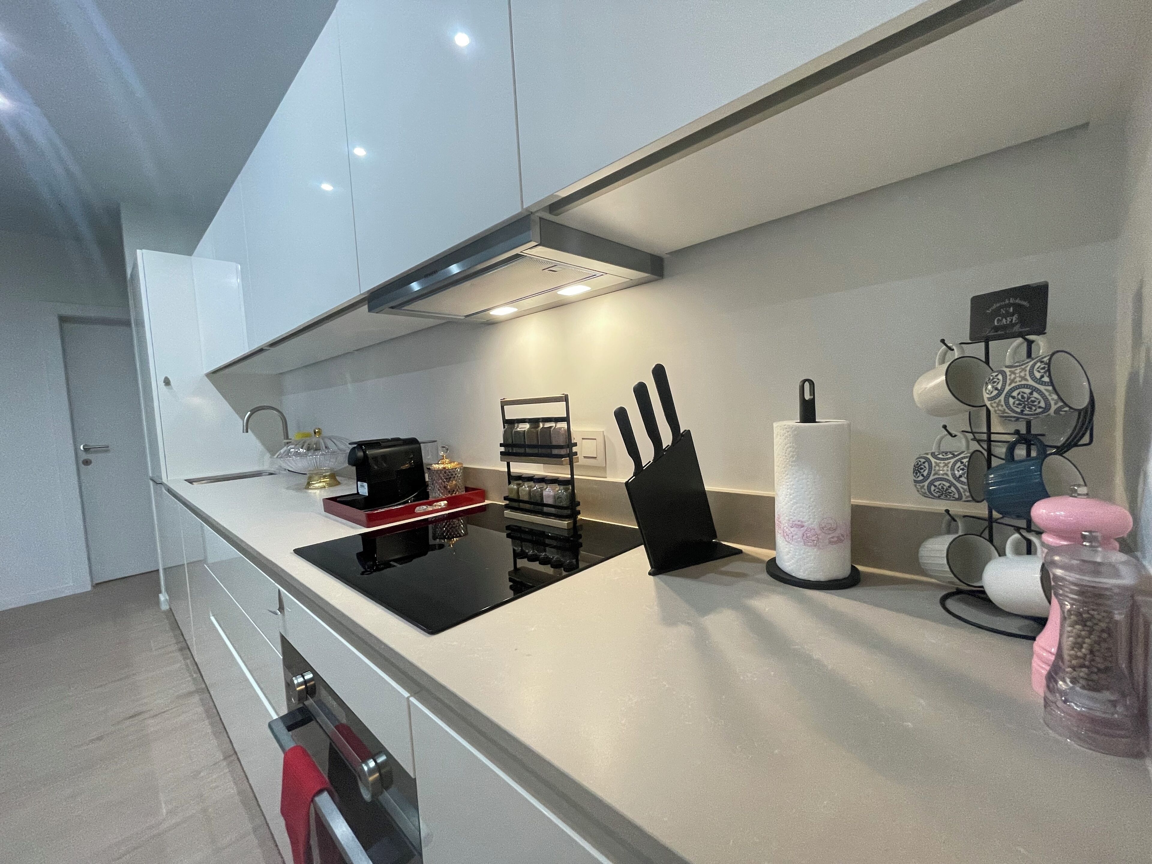 Una cocina moderna con armarios blancos, encimera negra, cafetera, bloque de cuchillos y un escurreplatos para tazas.