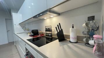 Una cocina moderna con armarios blancos, encimera negra, cafetera, bloque de cuchillos y un escurreplatos para tazas.
