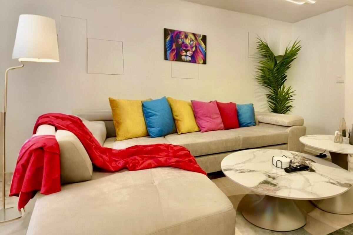 Un salon moderne avec un canapé beige, des coussins colorés, un plaid rouge, une table basse en marbre et un lampadaire.