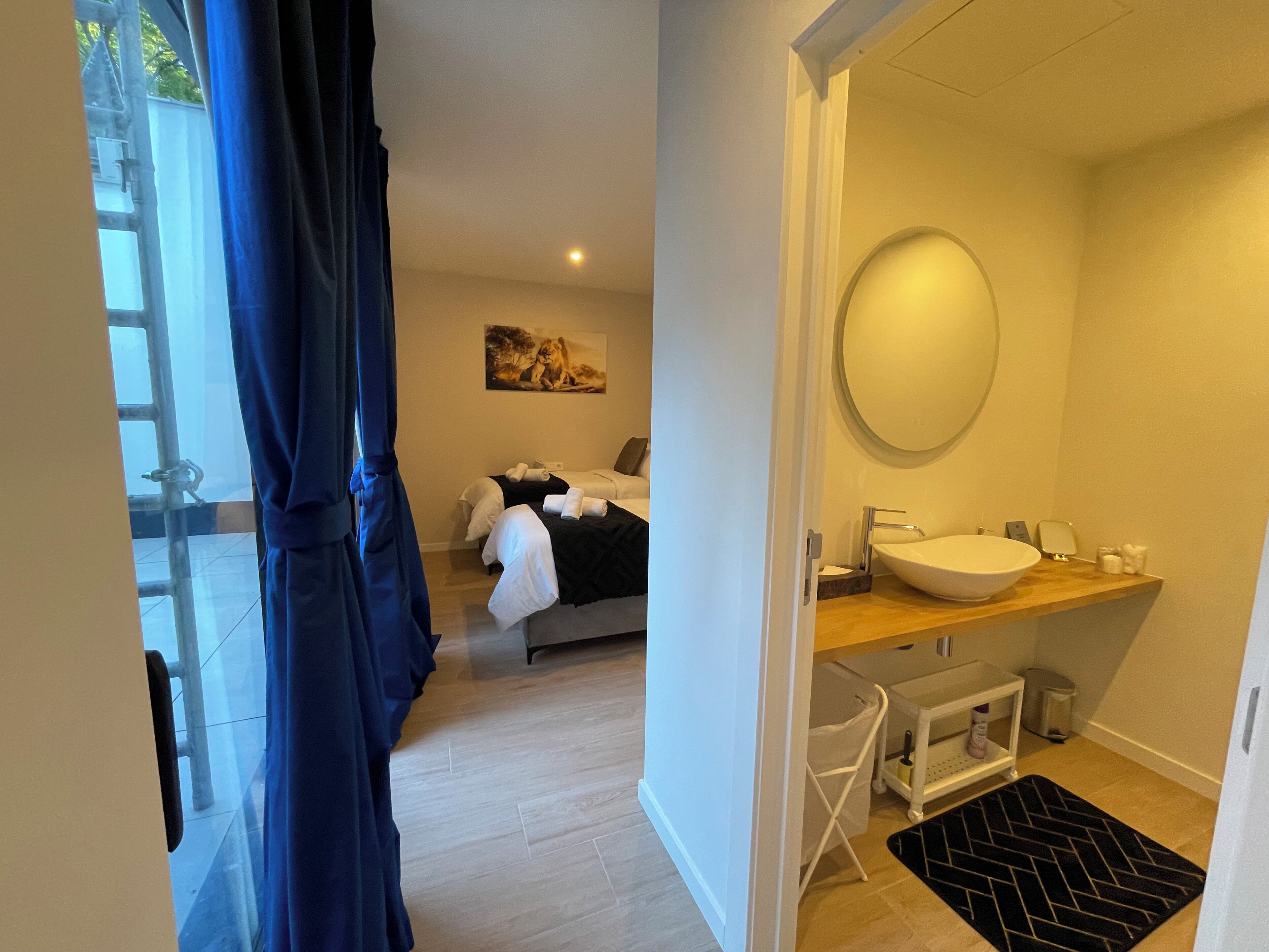 Une chambre d’hôtel moderne avec un grand lit, une salle de bain dotée d’un miroir rond et une vue sur l’extérieur grâce à une porte vitrée.