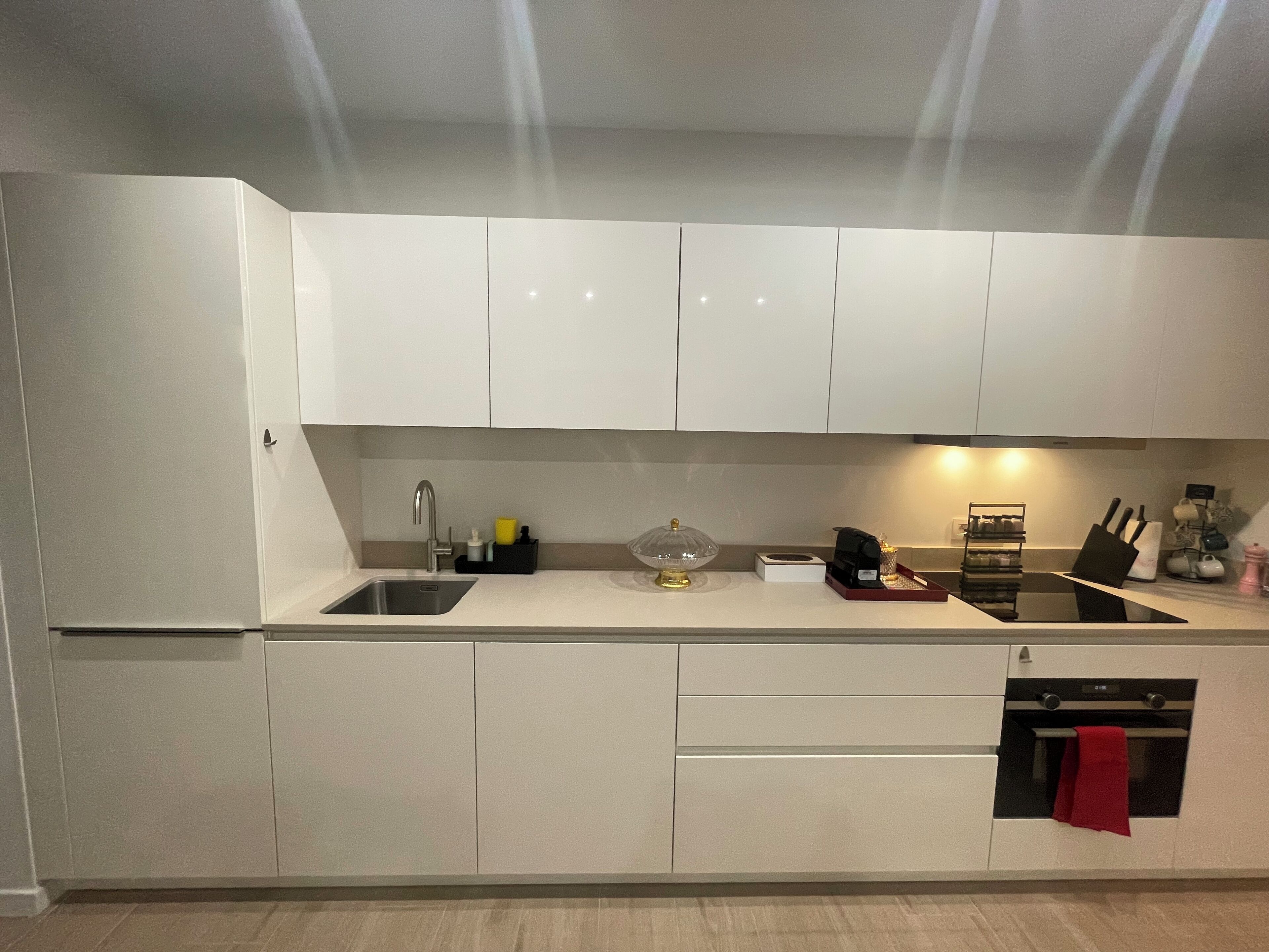 A modern kitchen with white cabinets, a stainless steel sink, and a built-in oven.