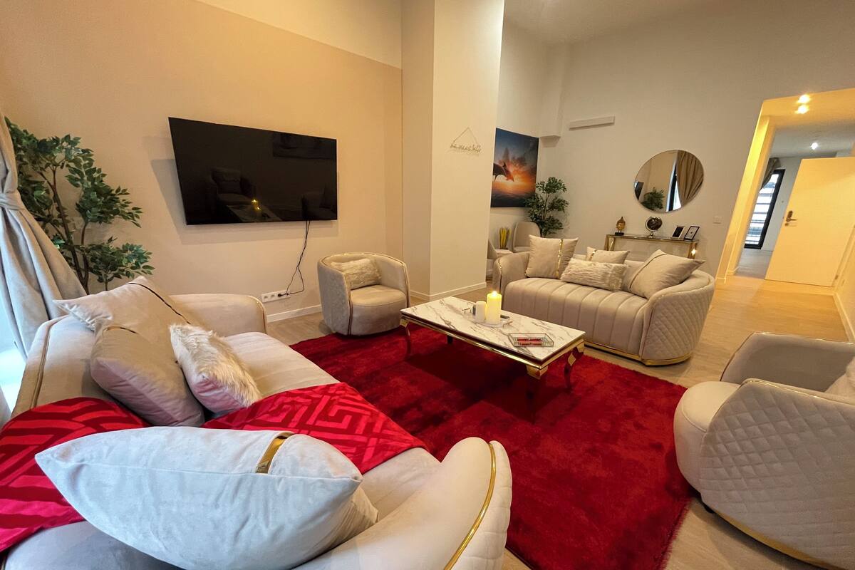 Un salon moderne avec une moquette rouge, des canapés blancs et un téléviseur à écran plat fixé au mur.