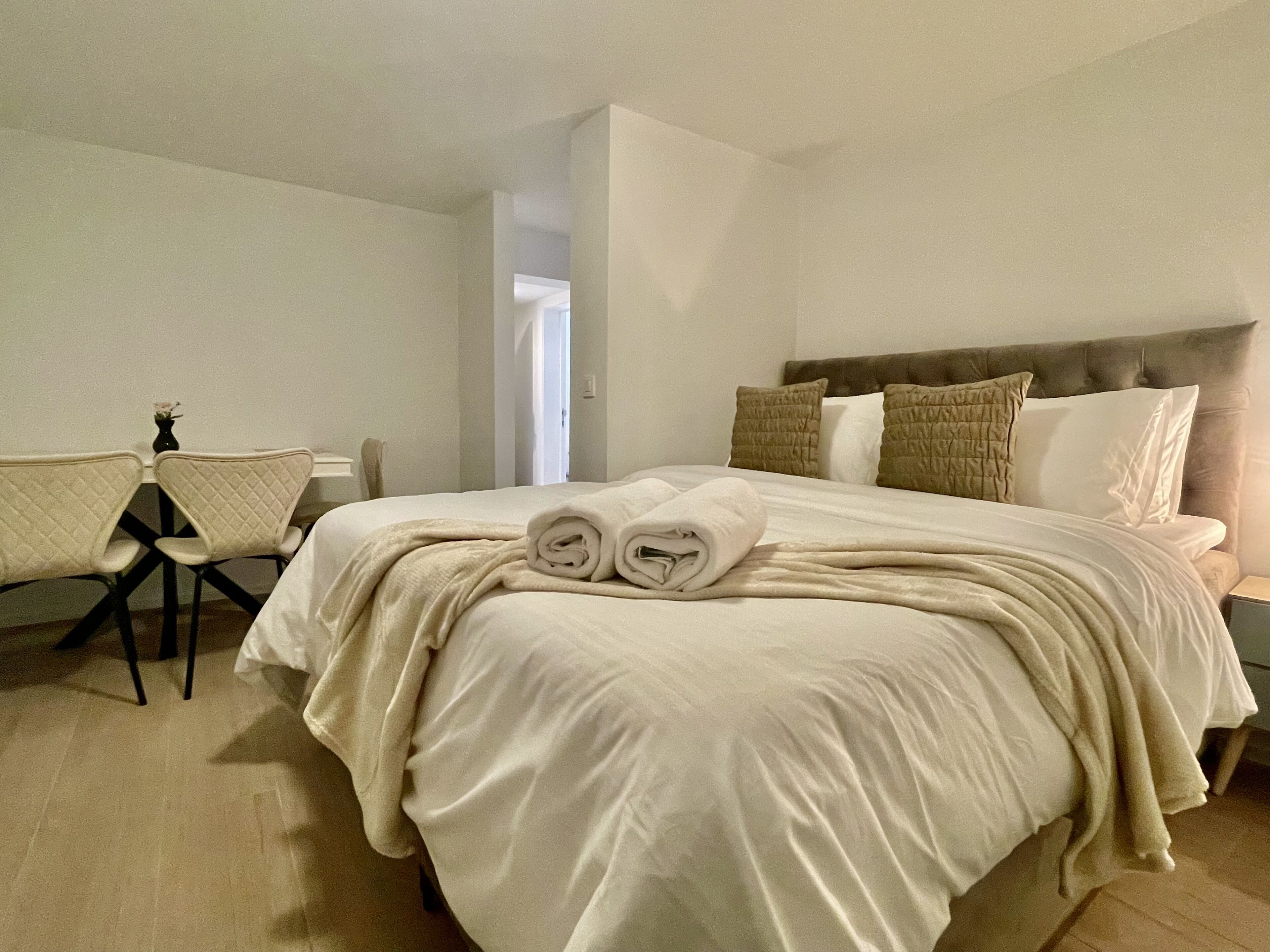 A hotel room with a large bed, a desk with a chair, and a small table with a vase.