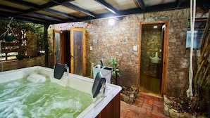 Un área de spa con una bañera de hidromasaje, puertas de madera, paredes de piedra y un lavamanos pequeño.