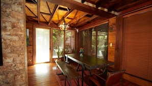 Un comedor de madera con una mesa, bancos, una araña y vistas al exterior.