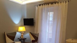 A hotel room with a bed, two chairs, a table with a lamp, a TV mounted on the wall, and a window with curtains. - Bellini house Sangiuliano 132 historic center Catania (Catania)