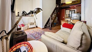 A cozy living room with a sofa, a lamp, a chair, and a staircase leading to a kitchen area.