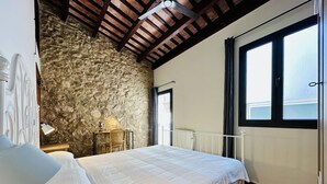 A bedroom with a stone wall, a large window, and a bed with a white bedspread.