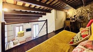 A rustic interior with exposed wooden beams, a staircase leading to a loft area, and a cozy seating area with a yellow rug and patterned pillows.