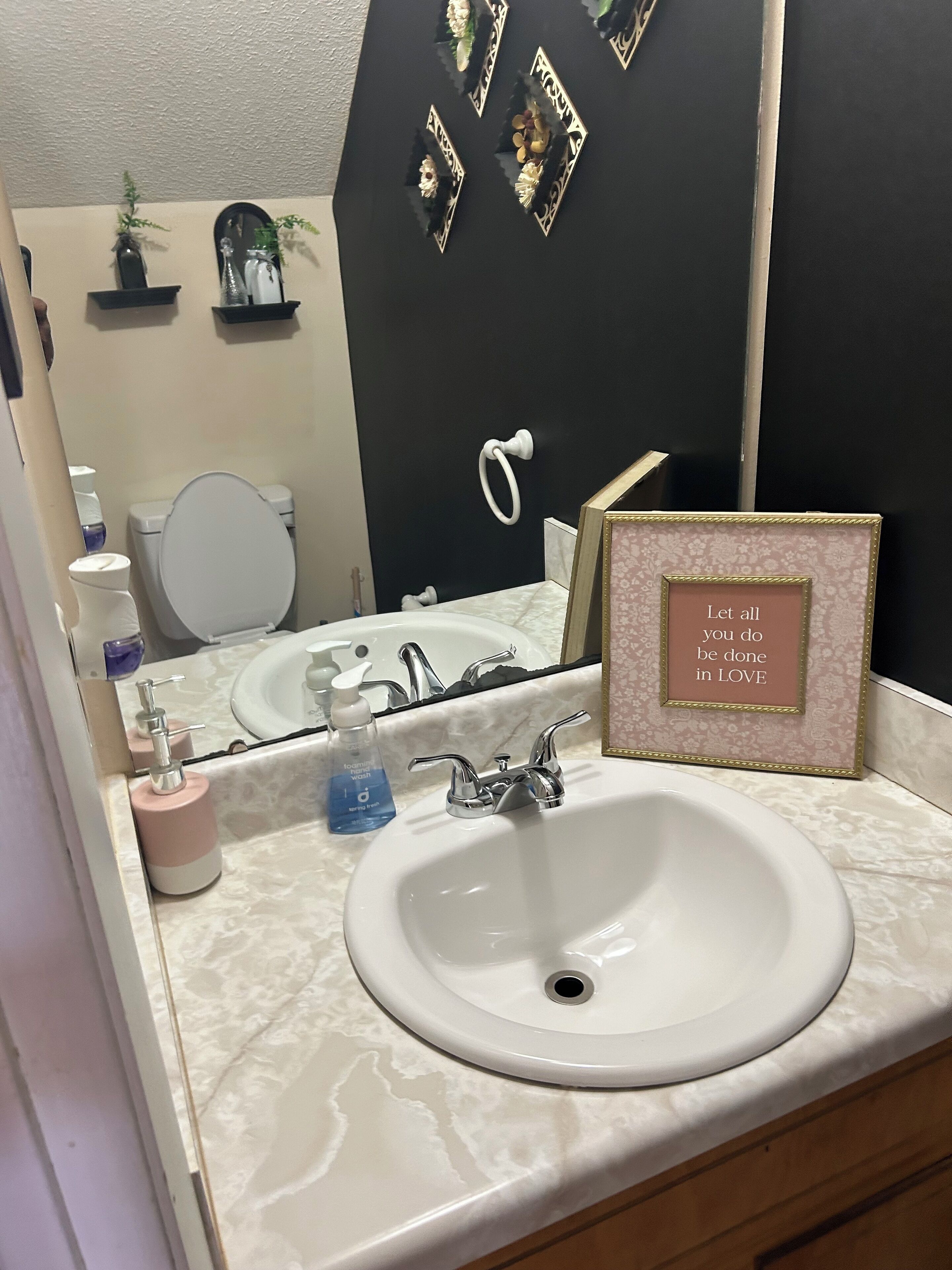 Un baño con un lavamanos blanco, un espejo, una cita inspiradora enmarcada y una pared negra con espejos decorativos.