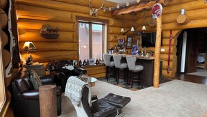 A log cabin interior with a bar area, leather seating, and rustic decor.