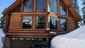 A log cabin with large windows, a garage, and a black SUV parked in front.