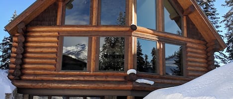 A log cabin with large windows, a garage, and a black SUV parked in front.