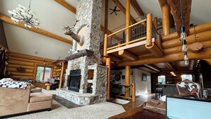 A log cabin interior with a stone fireplace, wooden beams, a sofa, and a laptop on a table.