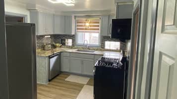 Una cocina con gabinetes grises claros, una estufa negra y una ventana con persianas.