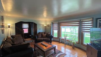 Amplia sala de estar con chimenea, asientos cómodos y ventanas grandes que ofrecen vistas al exterior.
