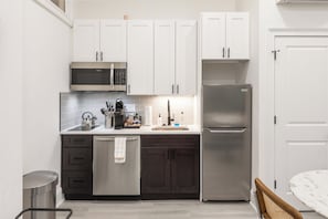 A modern kitchen with white cabinets, a stainless steel refrigerator, and a microwave. - Sosuite | 1BR Apt w W/D, Desk Alcove (Philadelphia)