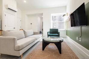 A modern living room with a sofa, a coffee table, and a television mounted on the wall. - Sosuite | 1BR Apt w W/D, Desk Alcove (Philadelphia)