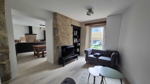 Un salon moderne avec un canapé gris, une petite table ronde et un téléviseur posé sur un meuble.
