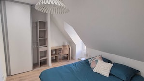Une chambre avec un plafond en pente, un lit avec une literie bleue, une chaise en bois, un bureau et une armoire.