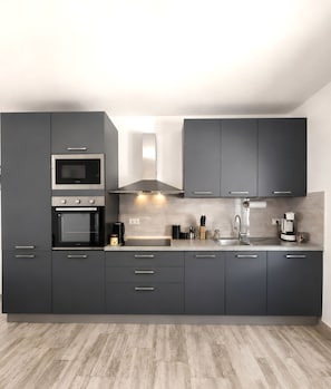 A modern kitchen with dark cabinets, a built-in oven, a microwave, a stainless steel sink, and a coffee maker.