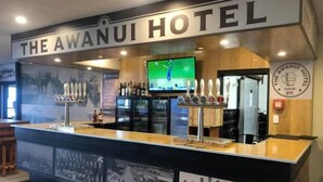 Zona de bar en el Hotel Awanui con televisor, grifos de cerveza y una exhibición de fotografías históricas.
