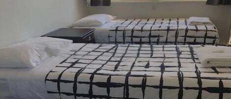 A room with two beds, each with a black and white checkered bedspread and white pillows. There is a window with blinds partially open, allowing natural light to enter.