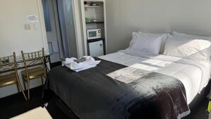 Una habitación de hotel con cama, un escritorio con sillas, un microondas y un mueble pequeño.