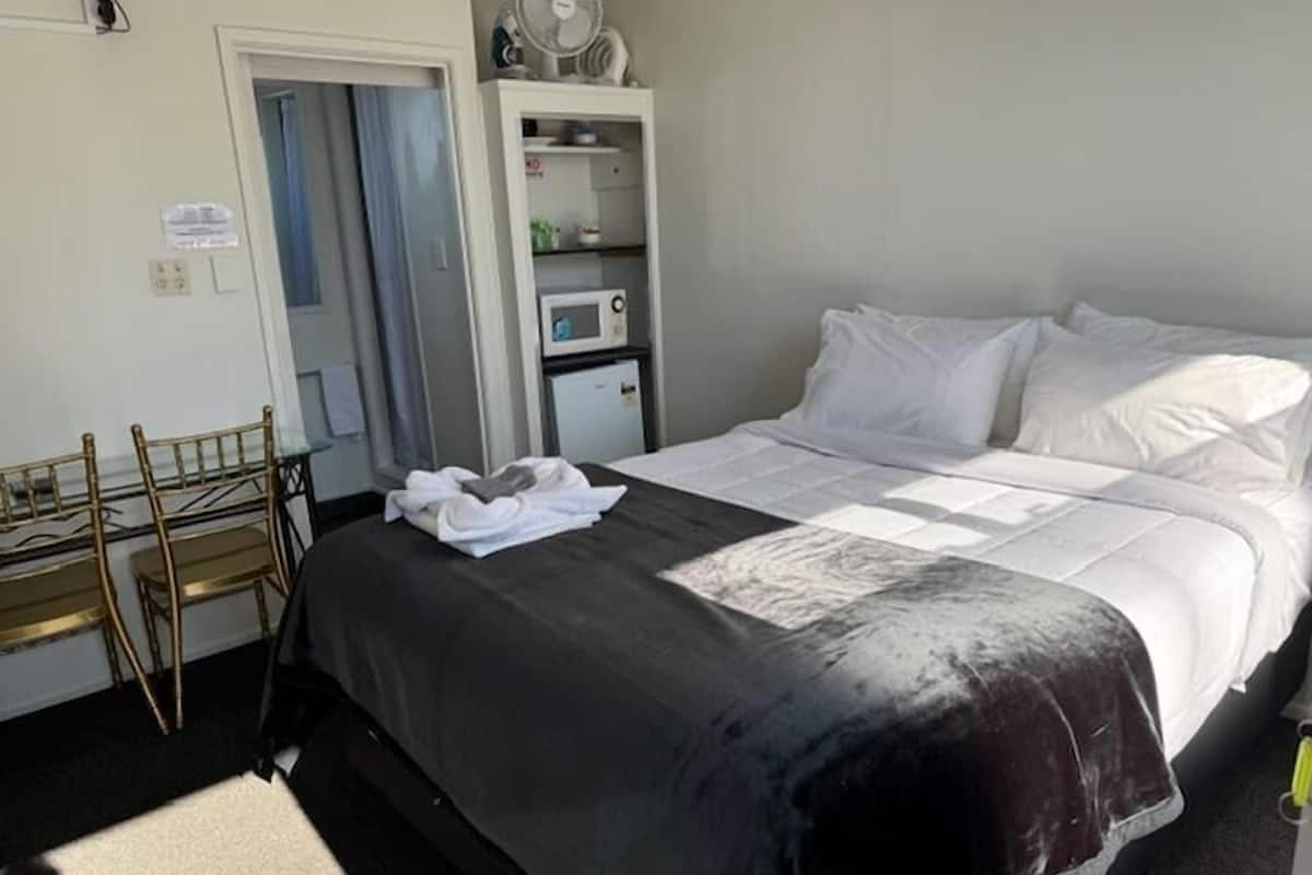 A hotel room with a bed, a desk with chairs, a microwave, and a small cabinet.