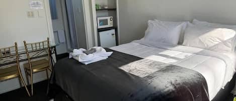 Una habitación de hotel con cama, un escritorio con sillas, un microondas y un mueble pequeño.