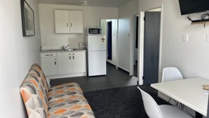 Una habitación compacta con kitchenette, un sofá, una mesa de comedor y un televisor instalado en la pared.