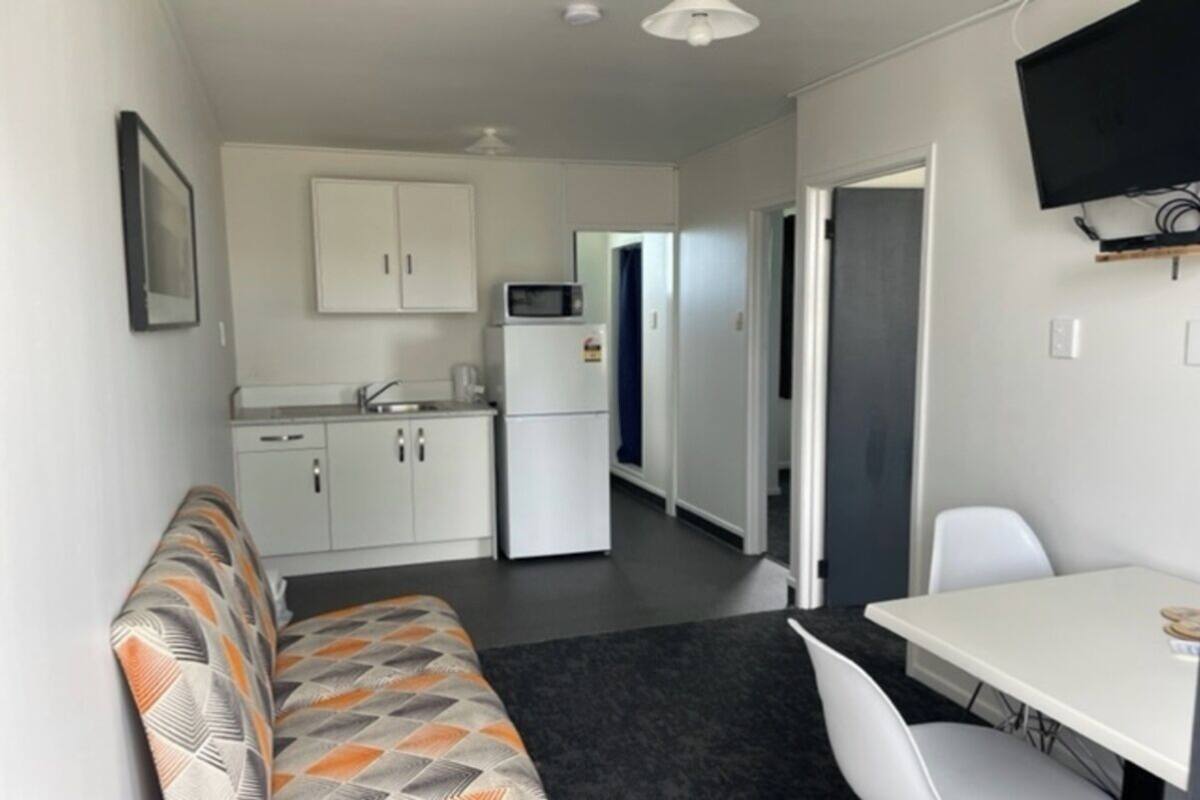 A compact room with a kitchenette, a sofa, a dining table, and a TV mounted on the wall.