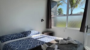 Un dormitorio con dos camas, una ventana con vista a palmeras y una pequeña mesa redonda.