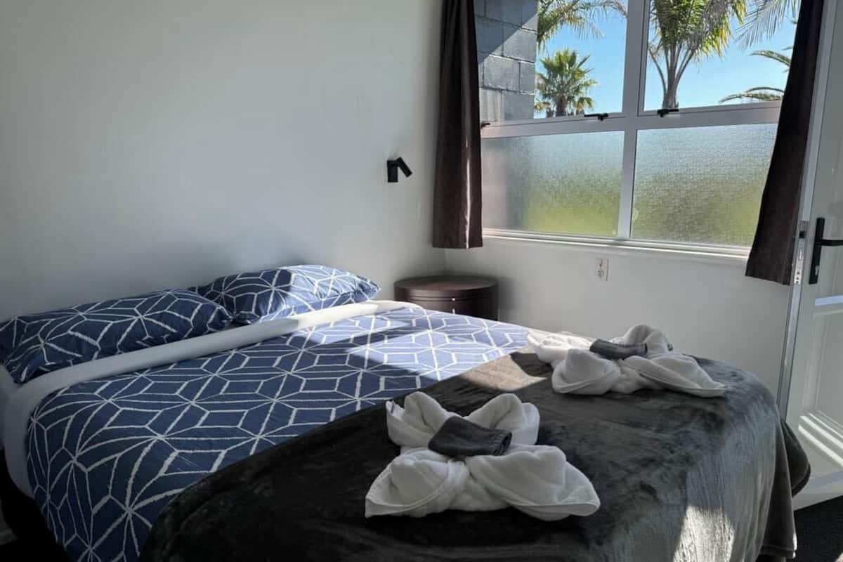 A bedroom with two beds, a window with a view of palm trees, and a small round table.