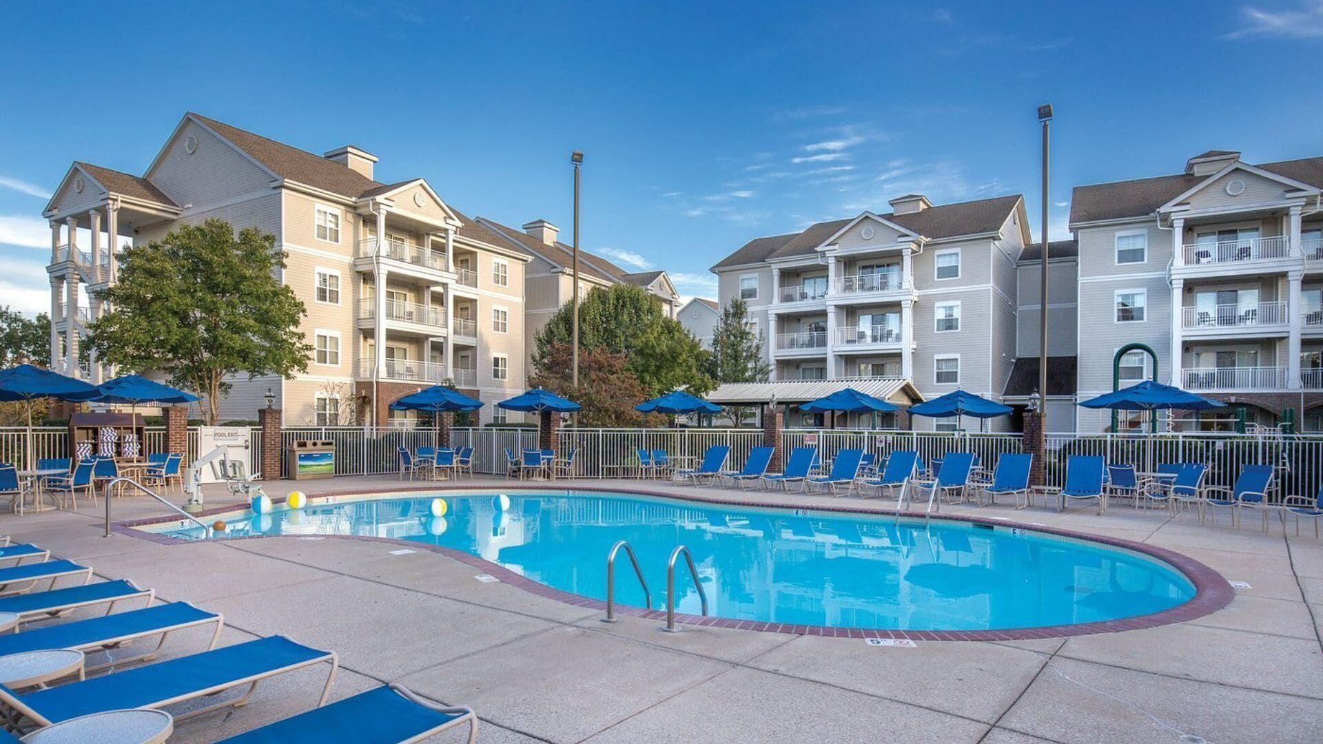 A swimming pool with lounge chairs and umbrellas, surrounded by multi-story buildings with balconies.