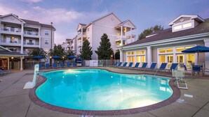 Une piscine entourée de bâtiments à plusieurs étages dotés de balcons, avec des chaises longues et des parasols à proximité.