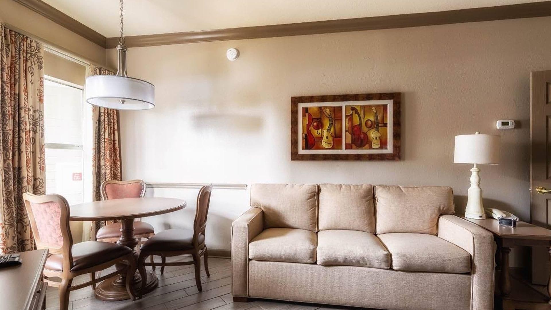 Una sala de estar con un sofá, una mesa redonda y dos sillas. Hay un cuadro en la pared y una lámpara sobre una mesita auxiliar.
