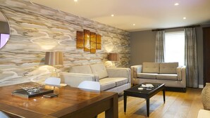 A modern living room with a stone wall, two sofas, a dining table, and a coffee table. - The Copper Horse Cottages (Scarborough)