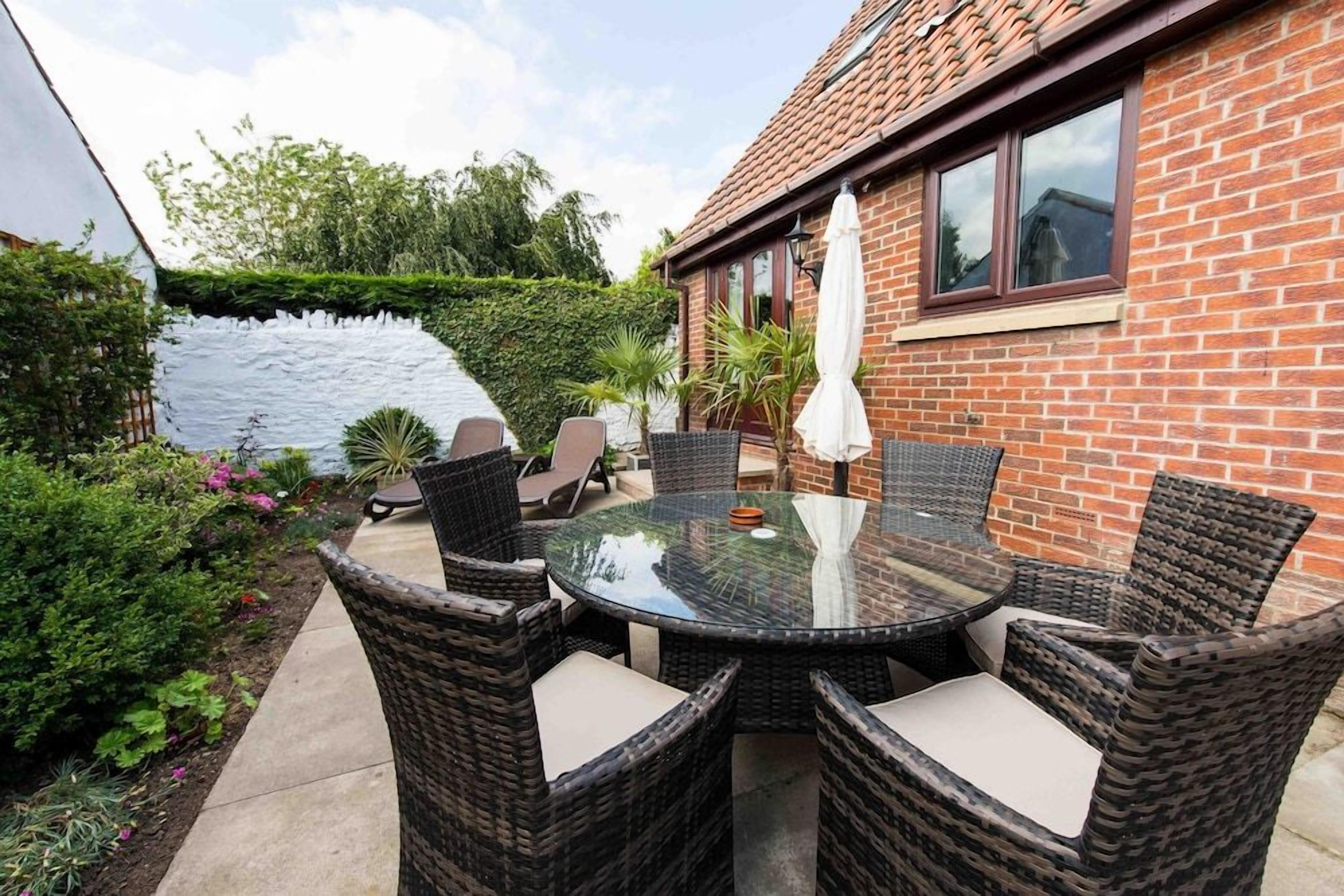 A patio with wicker furniture and a glass table, surrounded by a brick wall and greenery.
