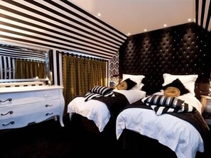 Quarto com parede listrada, cabeceira estofada e cómoda com gavetas.