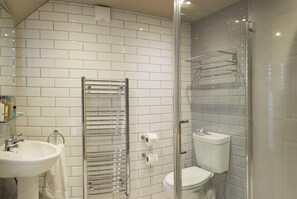 Un baño moderno con azulejos blancos tipo metro, una ducha con cerramiento de vidrio, un perchero de cromo y un lavamanos blanco.