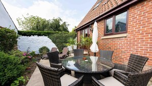 A patio with wicker chairs and a glass table, surrounded by a brick house and a white wall. - The Copper Horse Cottages (Scarborough)