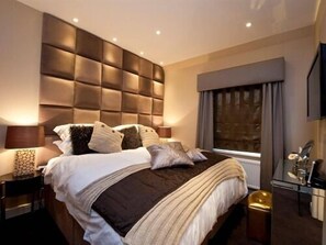 Quarto moderno com cabeceira estofada, uma janela grande com cortinas e uma mesinha de cabeceira com abajur.