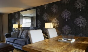 A room with a dark patterned wallpaper, a wooden dining table, a sofa, two lamps, and a mirror.