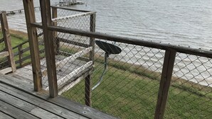 A wooden deck with a chain-link fence overlooking a calm body of water. - Charming 2-bedroom house with a beautiful view, WiFi, AC in Olivia (Port Lavaca)