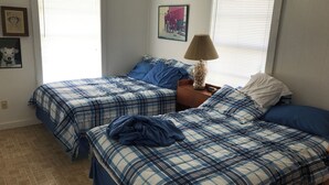 A bedroom with two beds, each with blue and white checkered bedding, a nightstand with a lamp, and a framed picture on the wall. - Charming 2-bedroom house with a beautiful view, WiFi, AC in Olivia (Port Lavaca)
