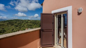 Un balcon doté d’une porte en bois, d’une porte vitrée et offrant une vue sur une colline verdoyante.