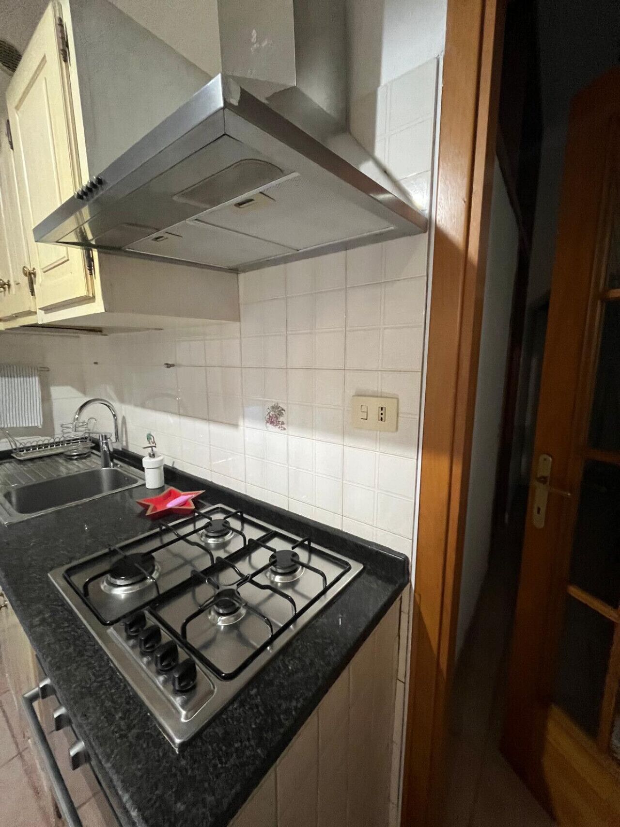 Een kleine keuken met een gasfornuis, een spoelbak en witte betegelde wanden.